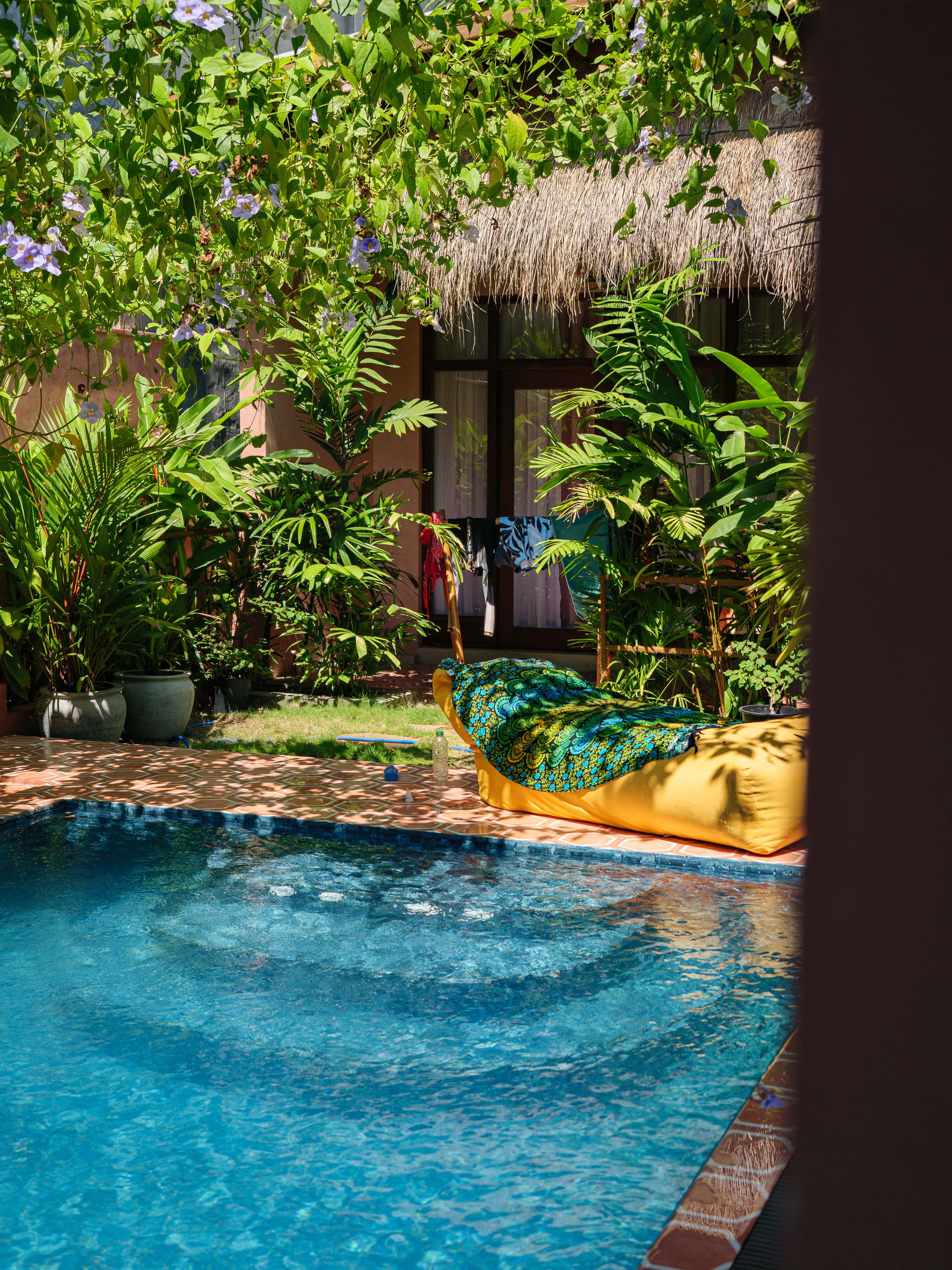 Sunny swimming pool area with a bean bag lounge chair and thatched roof bungalow at Pine and Palm in Arugam Bay