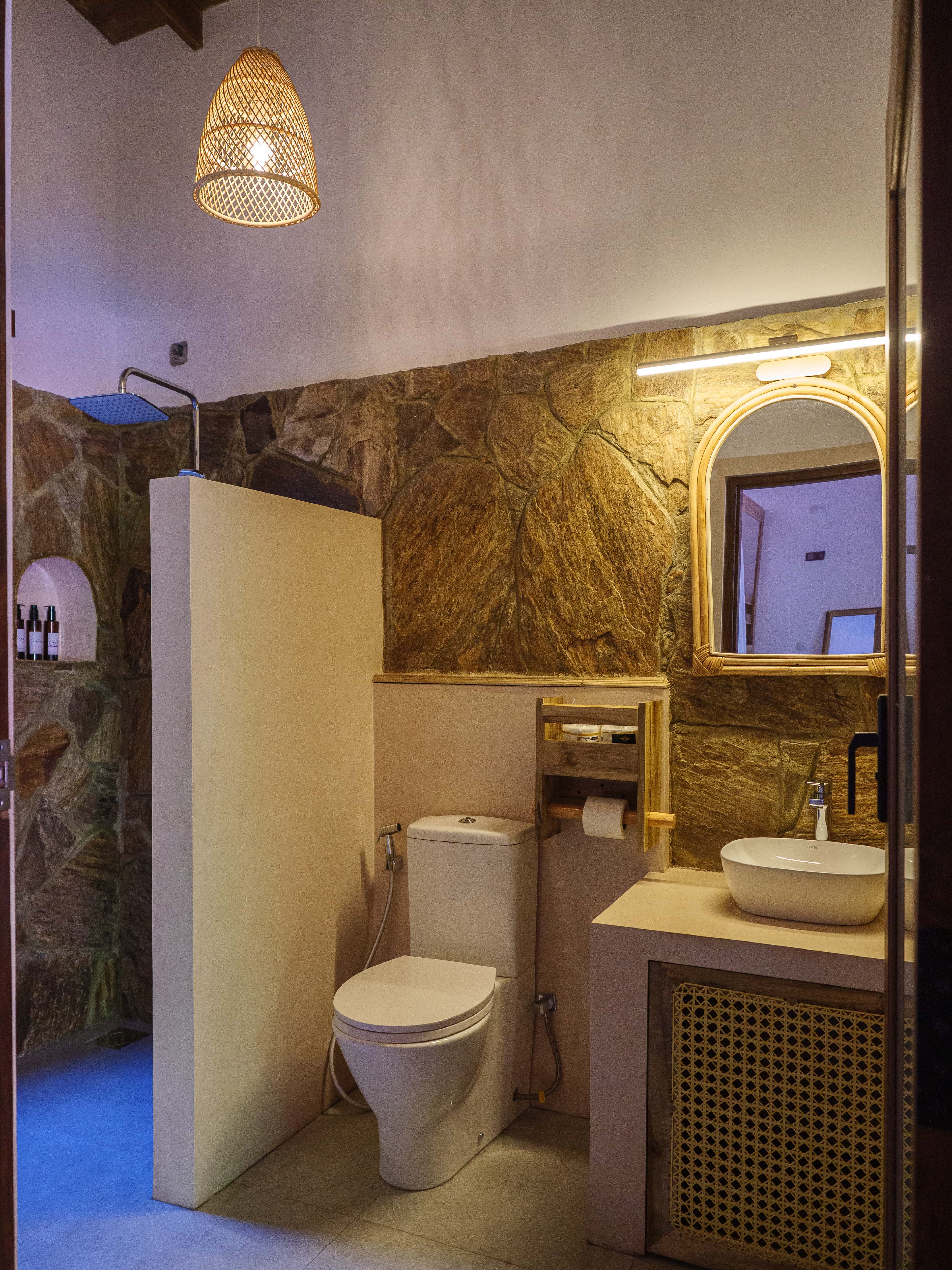Spacious ensuite bathroom with natural stone walls, rainfall shower, and wicker pendant light at Pine and Palm in Arugam Bay