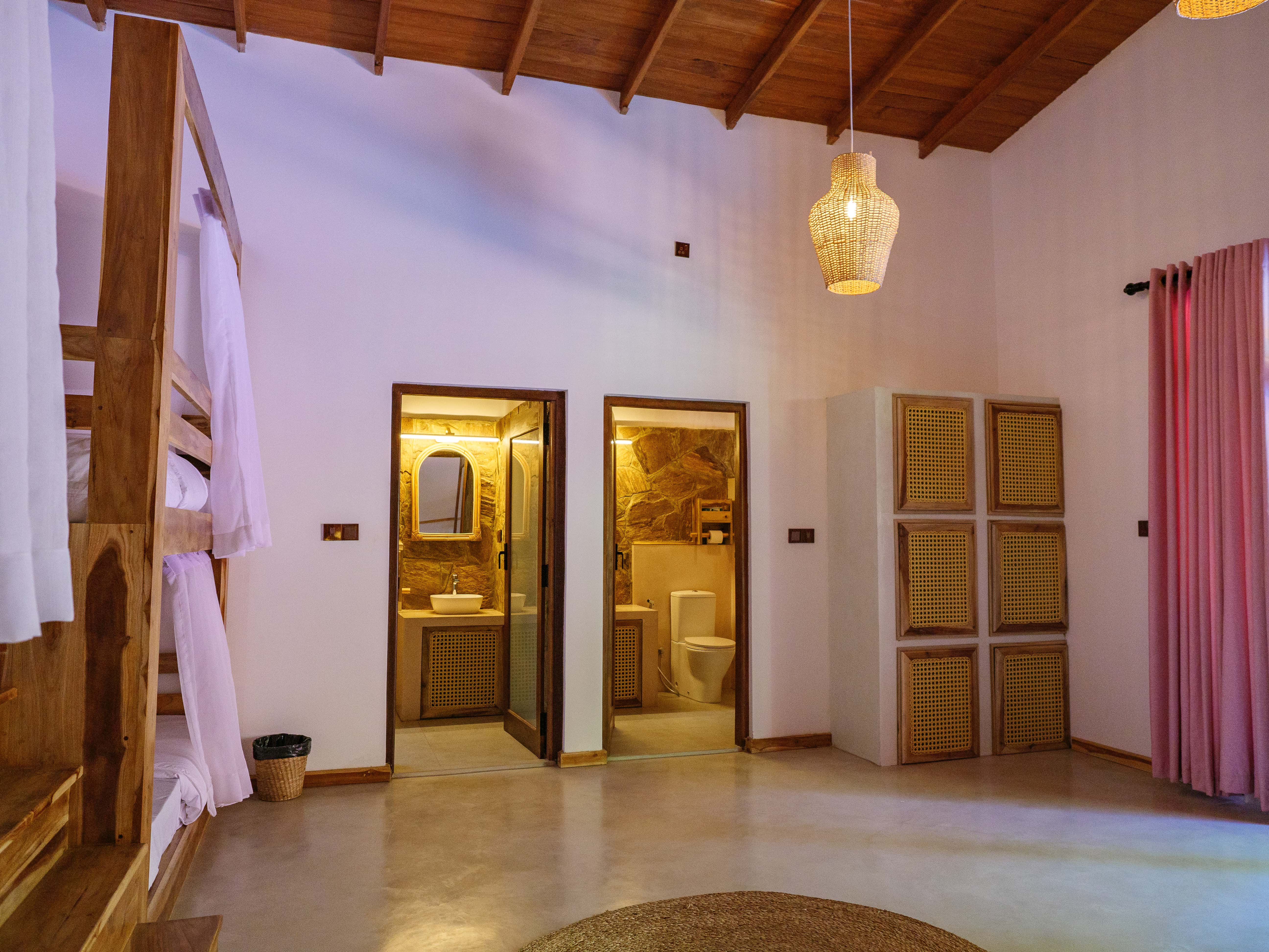 Spacious shared dorm room at Pine and Palm in Arugam Bay showing two ensuite bathrooms, a woven wicker wardrobe, and wooden bunk beds
