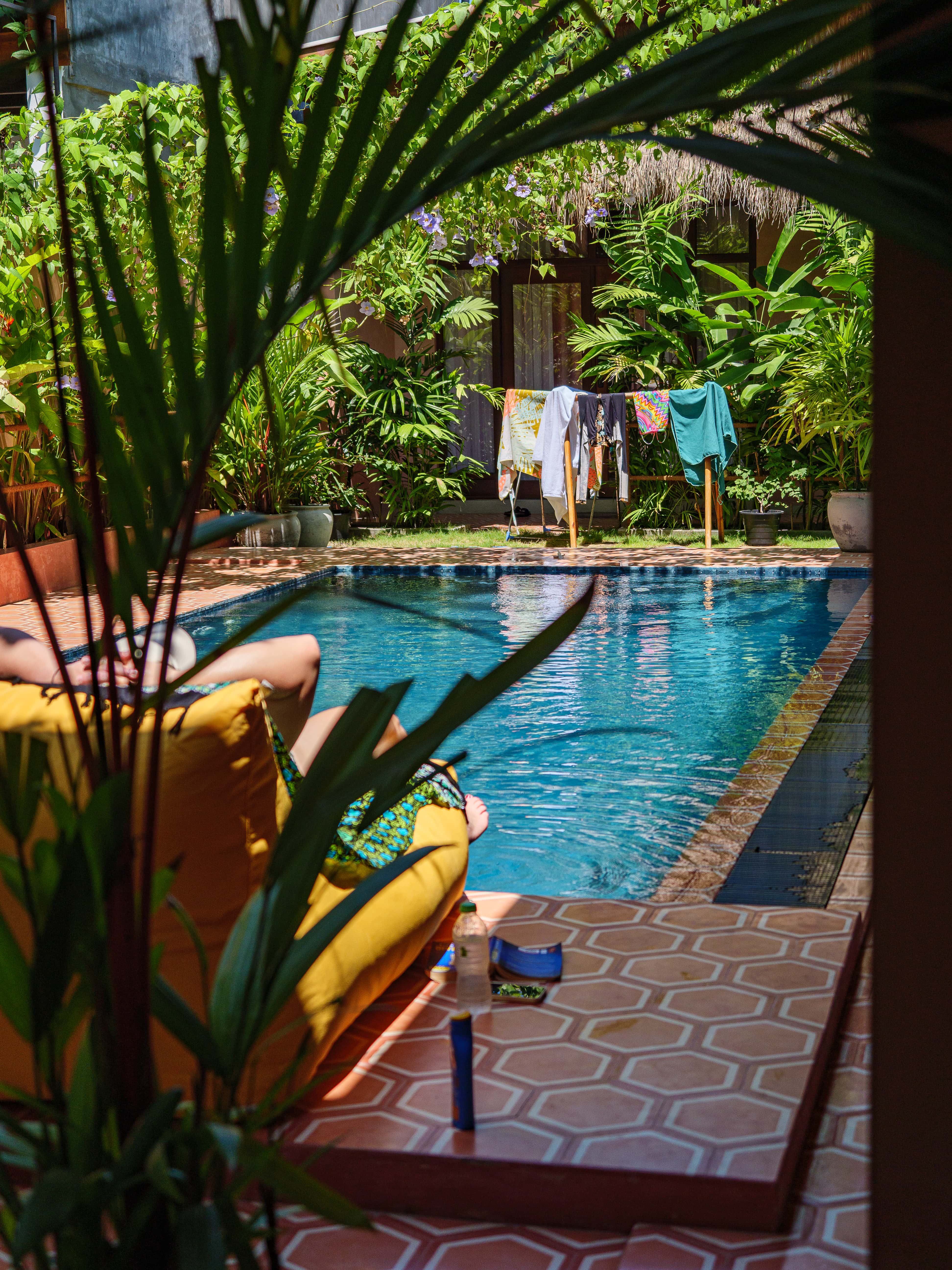 Relaxing poolside view through green leaves with a person lounging on a yellow bean bag by the swimming pool at Pine and Palm in Arugam Bay