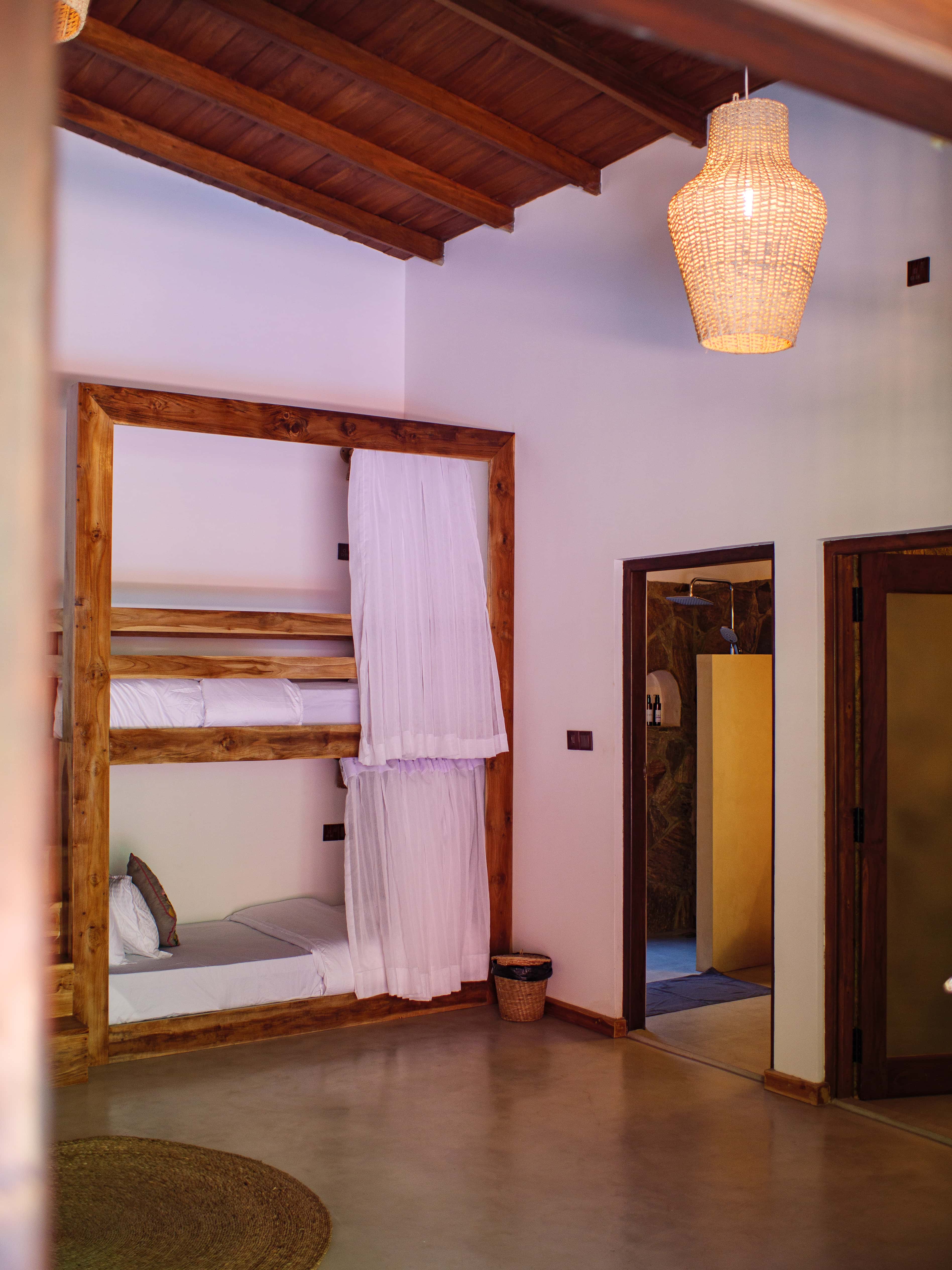 Bright six-bed dorm room with wooden bunk beds, white privacy curtains, and a round jute rug at Pine and Palm in Arugam Bay