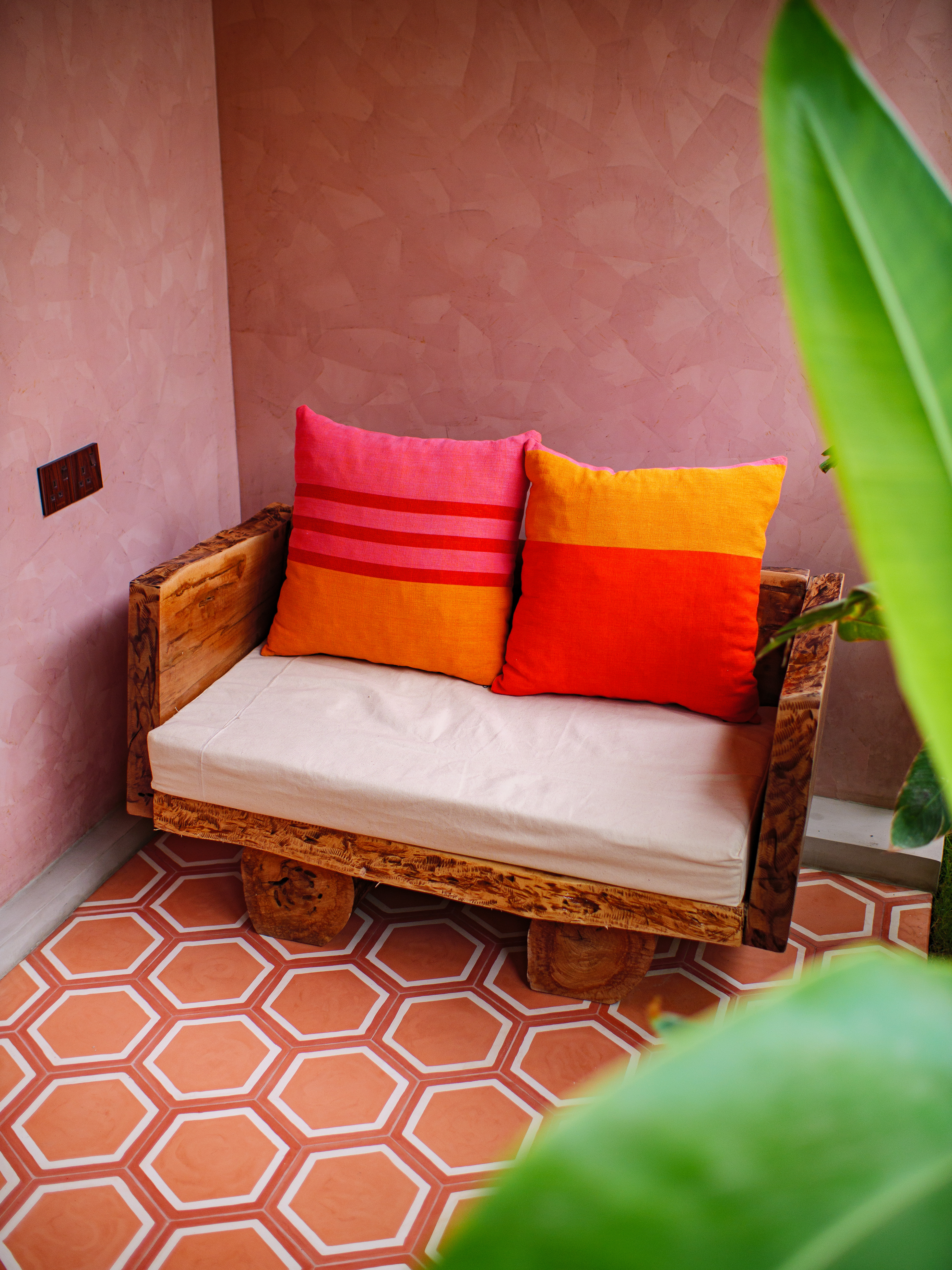 Rustic wooden bench with vibrant pink and orange pillows on a private terrace at Pine and Palm double room in Arugam Bay
