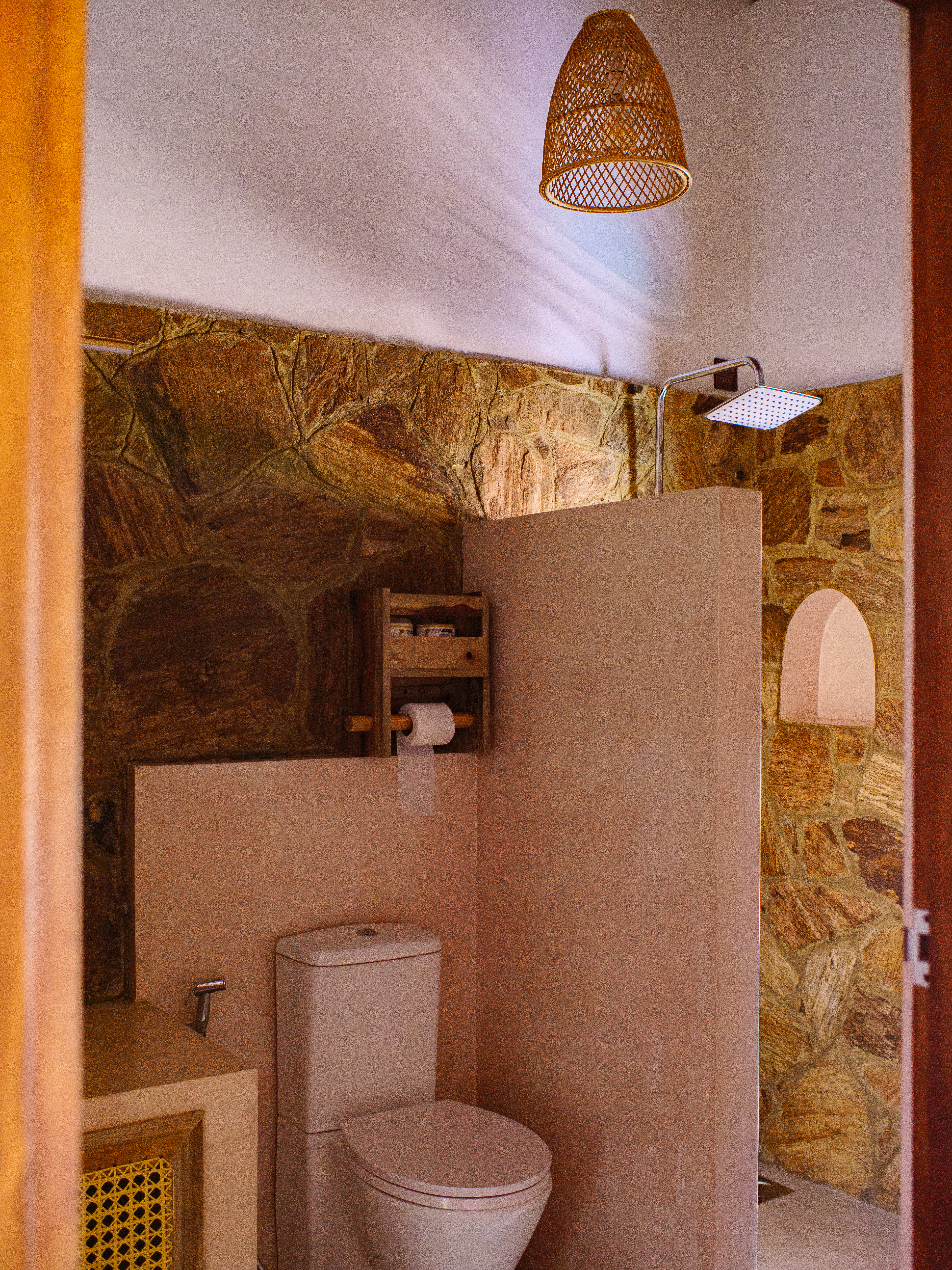 Ensuite bathroom with natural stone walls, a rainfall shower head, and rustic wooden fixtures at Pine and Palm in Arugam Bay